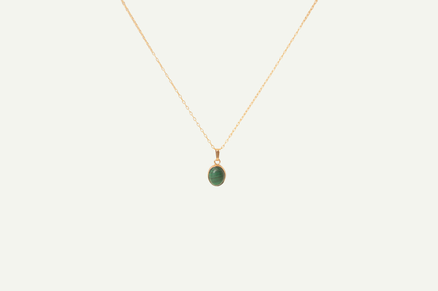Gold necklace with a green malachite pendant on a beige background