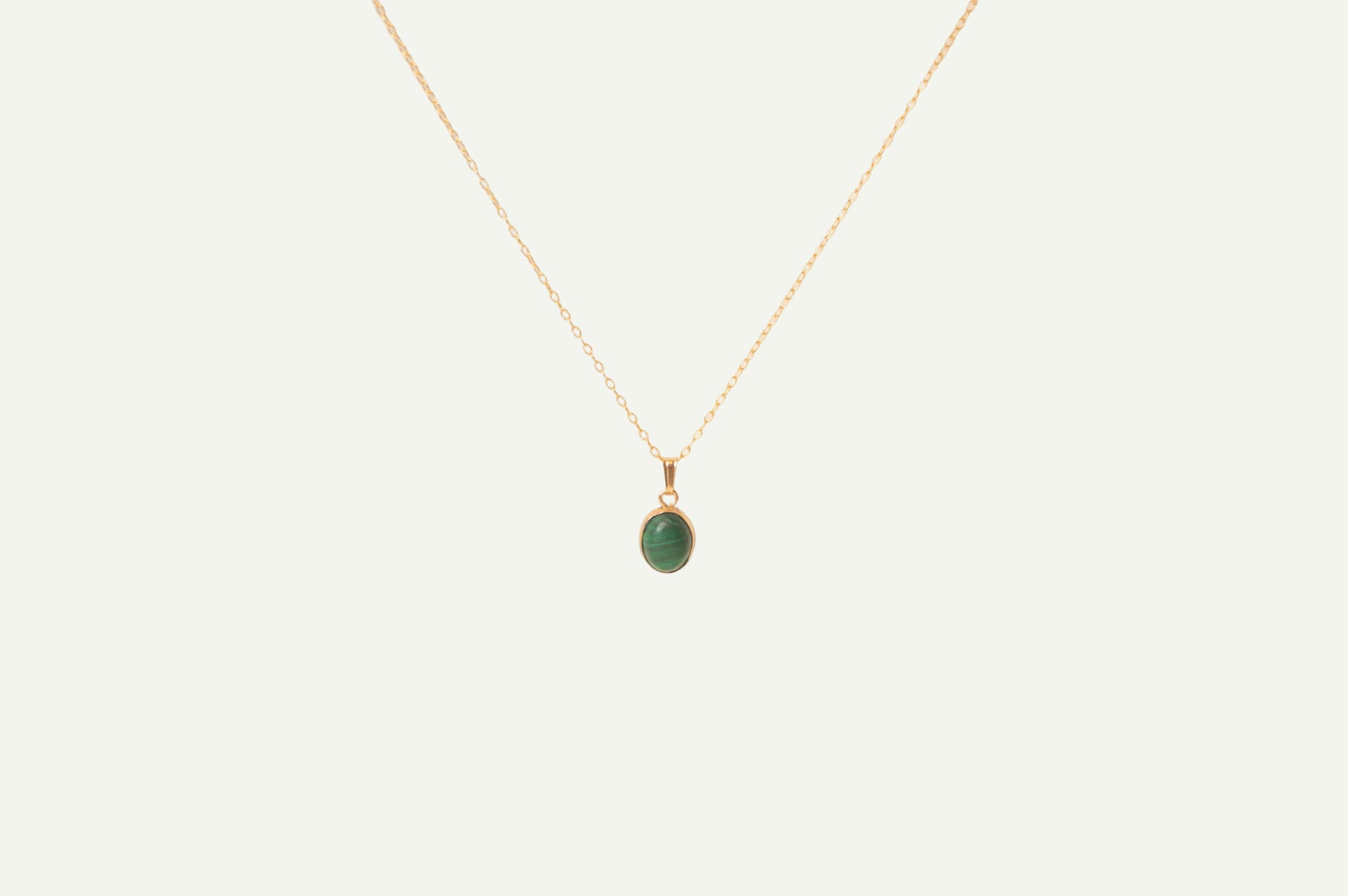 Gold necklace with a green malachite pendant on a beige background