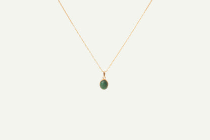 Gold necklace with a green malachite pendant on a beige background