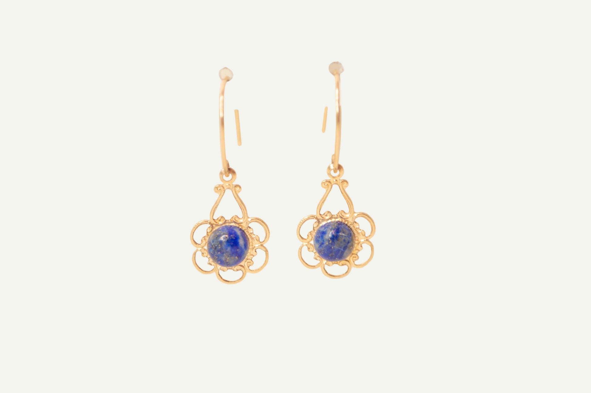 Gold earrings with blue lapis gemstones on a beige background