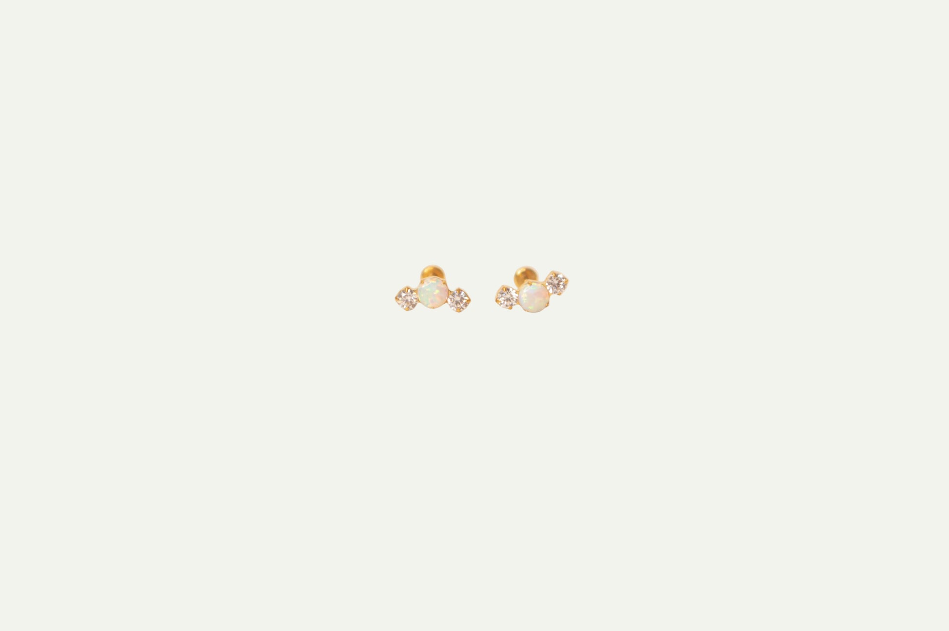 Pair of gold flatback earrings with opal and crystals on a beige background