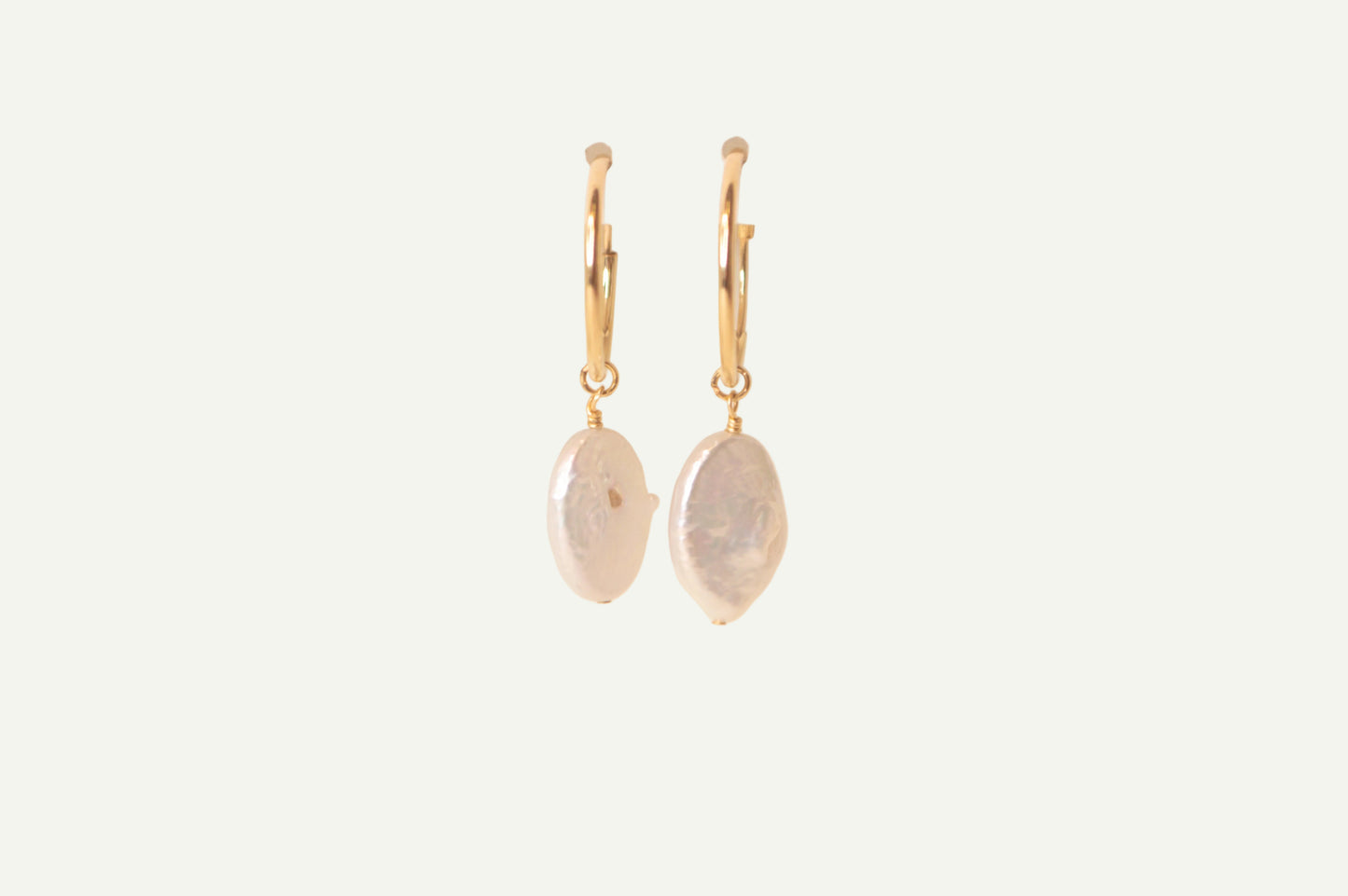 Pair of gold earrings with oval pearls on a beige background