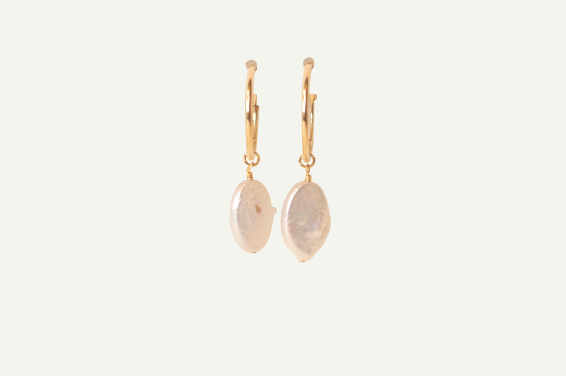 Pair of gold earrings with oval pearls on a beige background