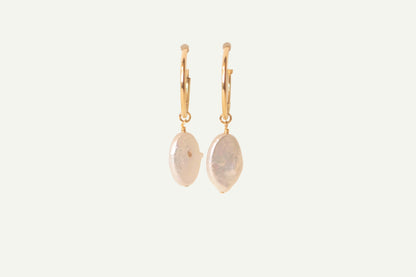 Pair of gold earrings with oval pearls on a beige background