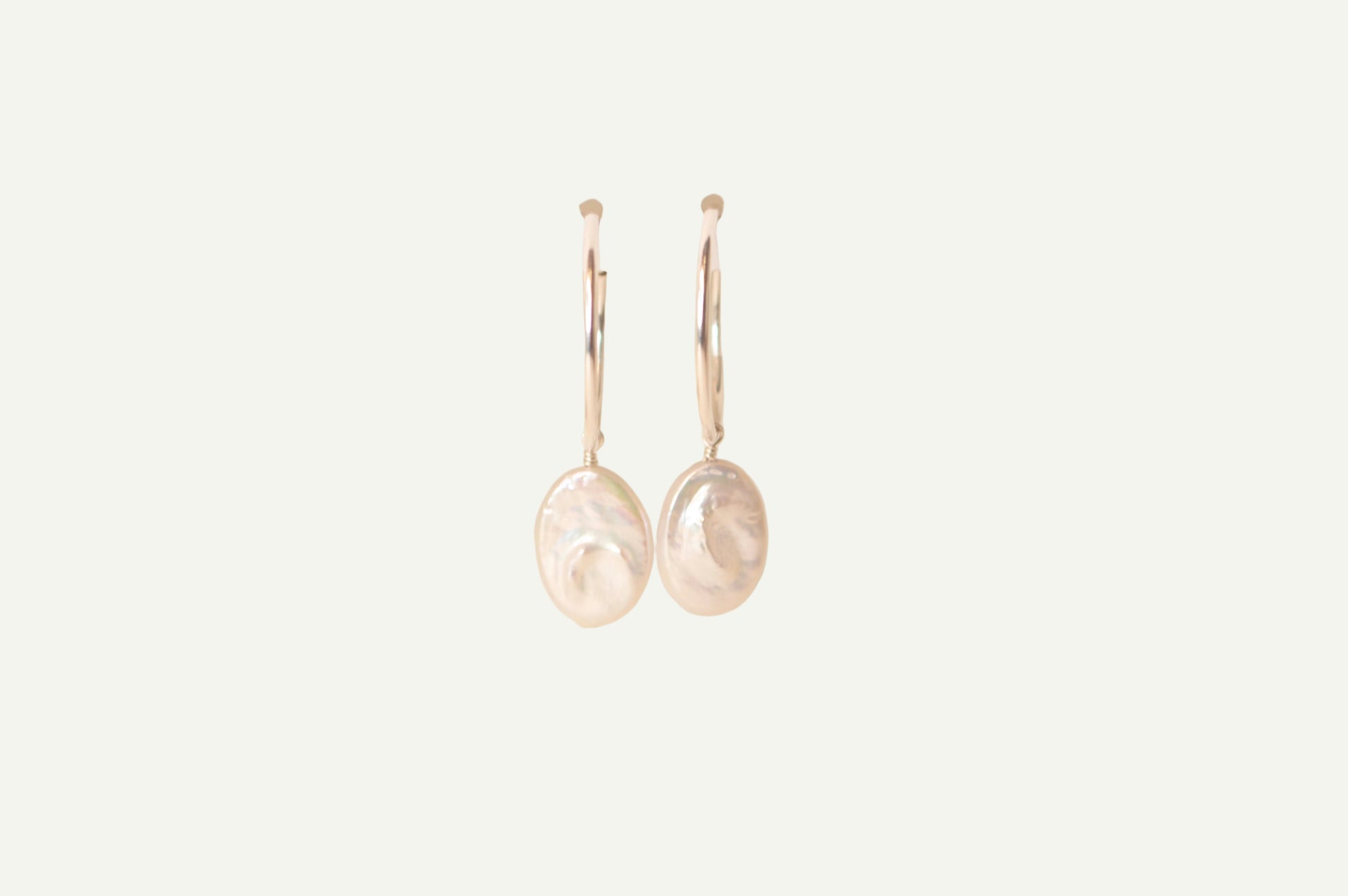Pair of oval pearl earrings on a beige background