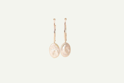 Pair of oval pearl earrings on a beige background