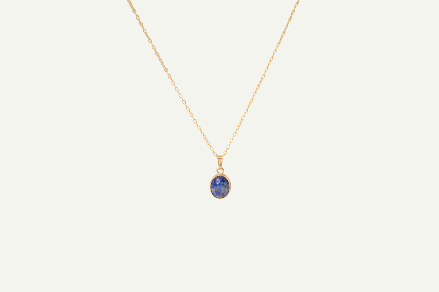 Gold necklace with a blue lapis pendant on a beige background