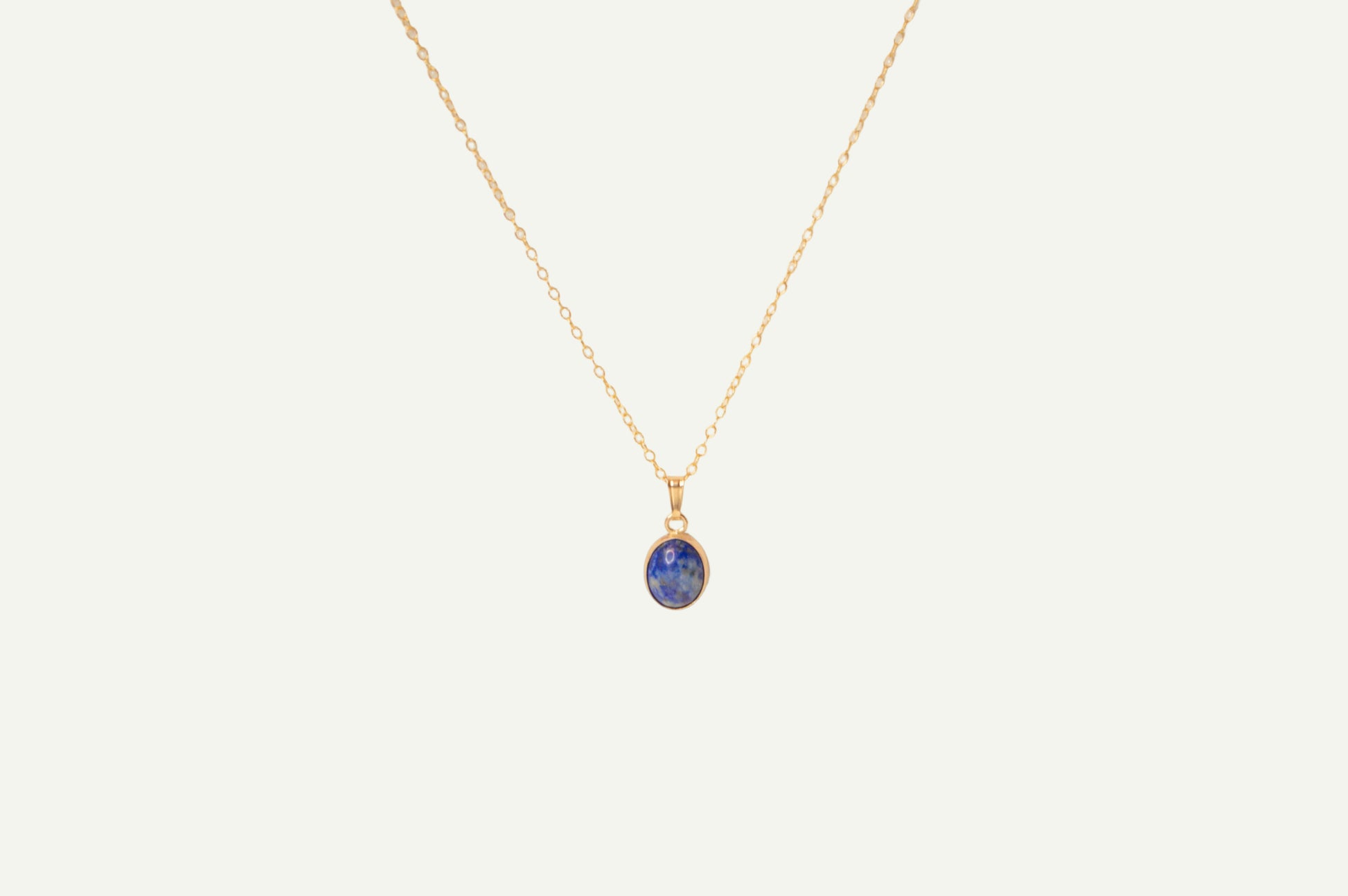 Gold necklace with a blue lapis pendant on a beige background