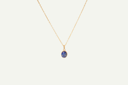 Gold necklace with a blue lapis pendant on a beige background