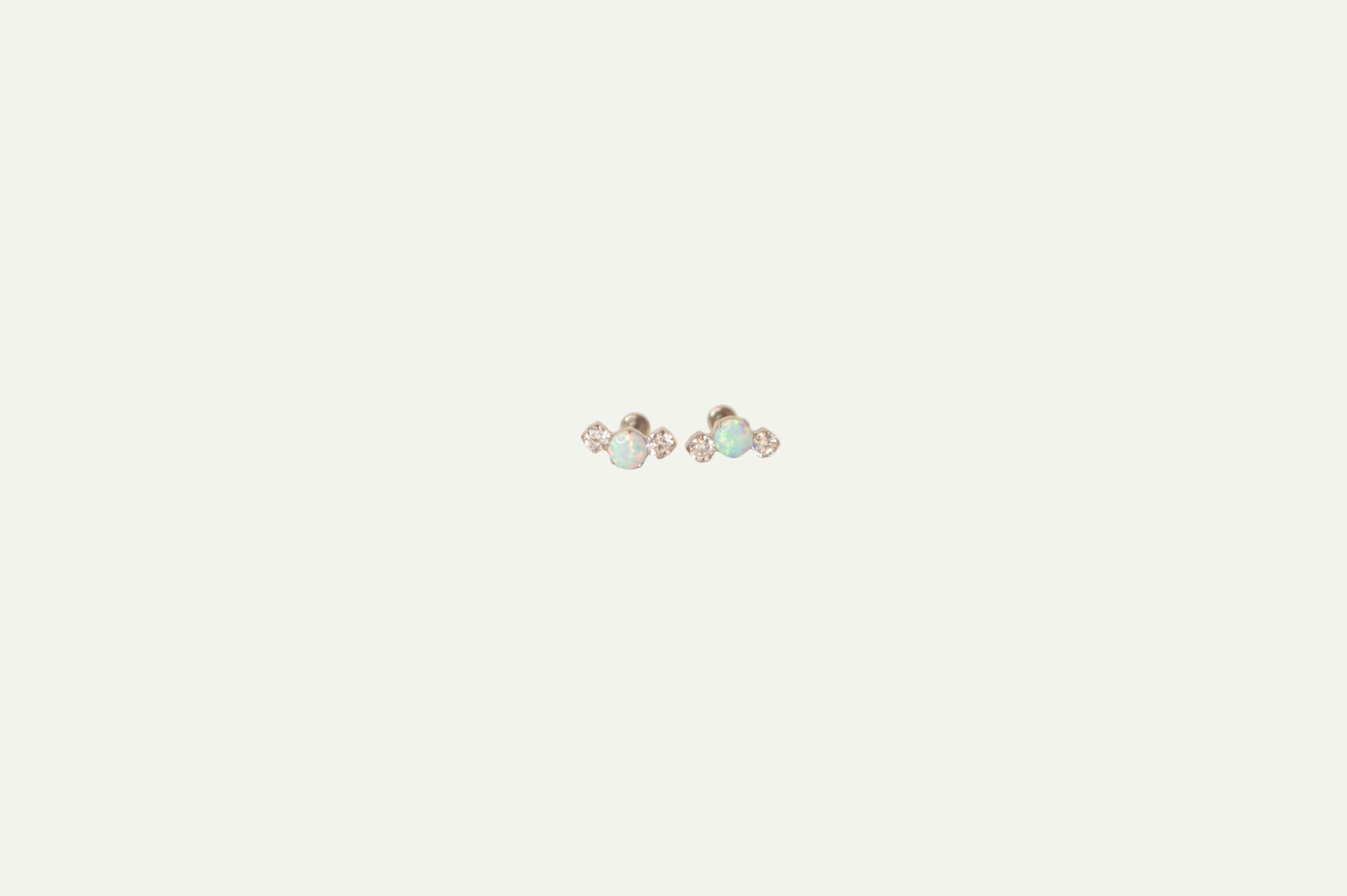 Pair of silver flatback earrings with Opal and crystals on a beige background