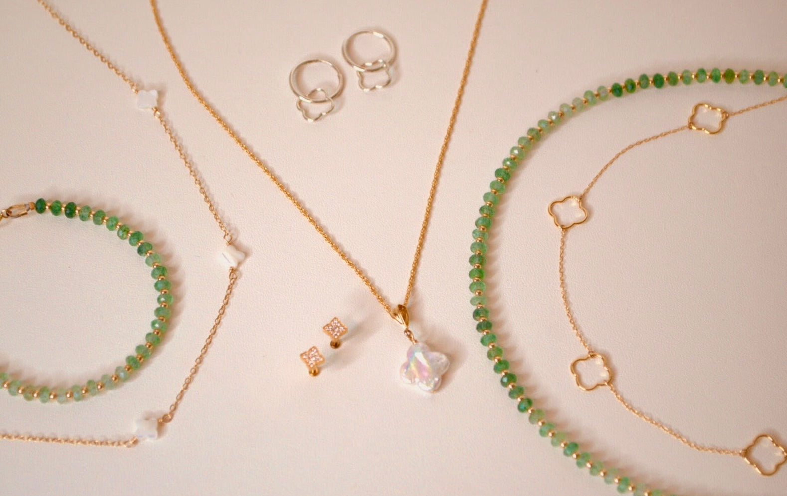 Jewelry set including clover necklaces, bracelets, and earrings on a light background