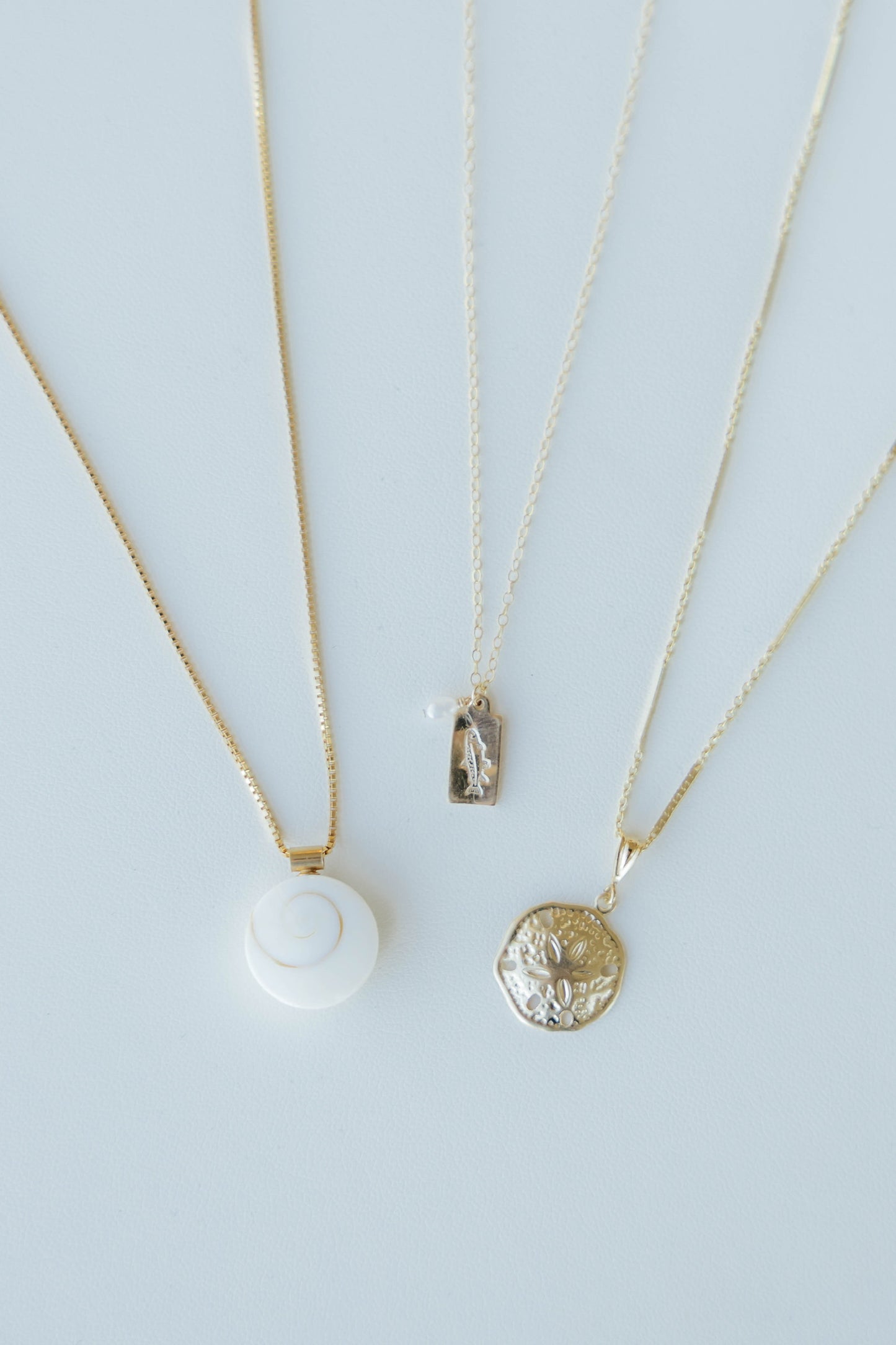 Three gold necklaces with pendants on a light blue background