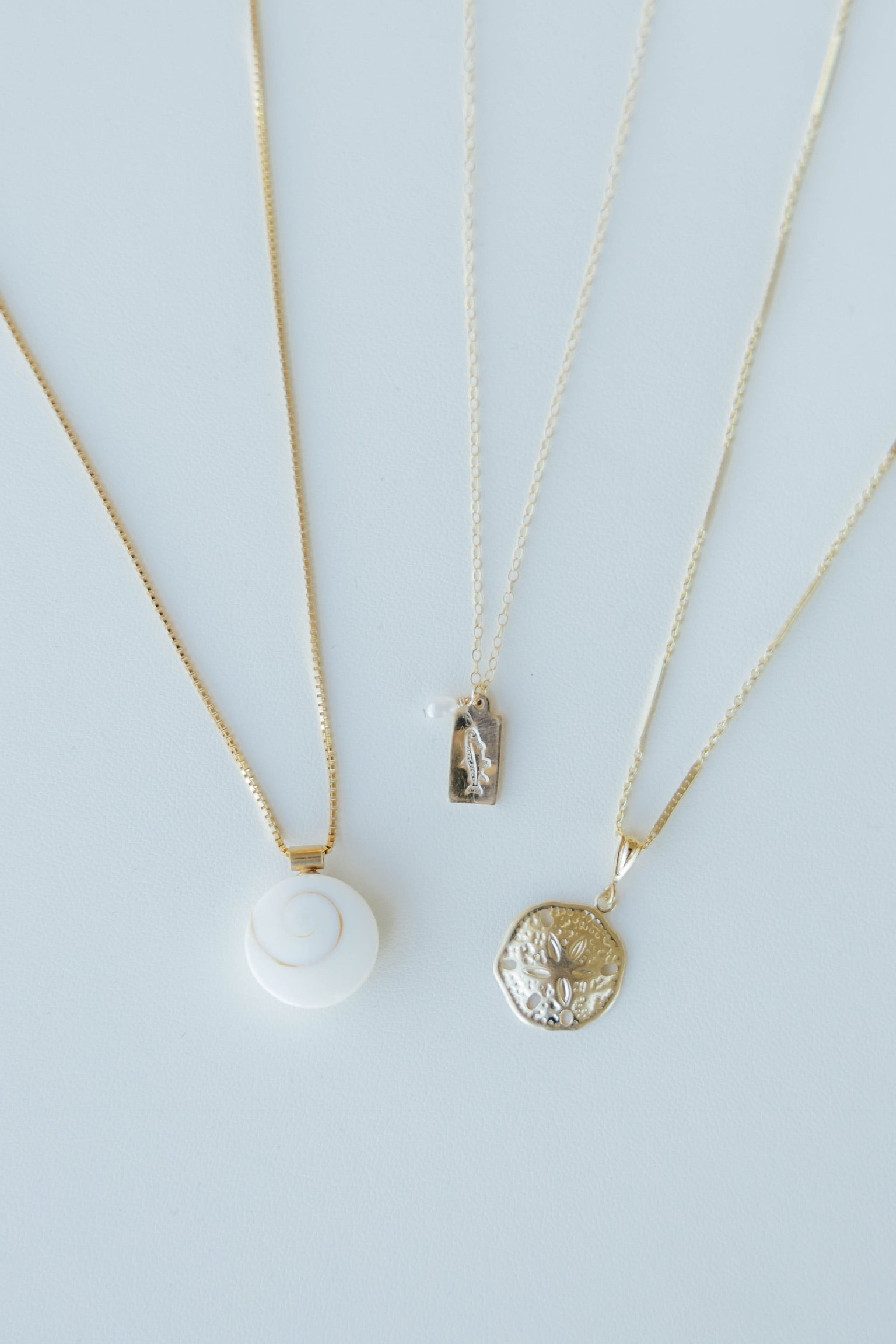 Three gold necklaces with pendants on a light blue background