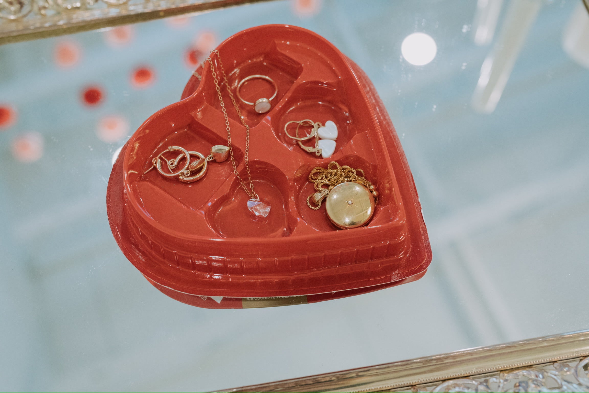 Heart-shaped jewelry box with gold necklaces and rings on a reflective surface