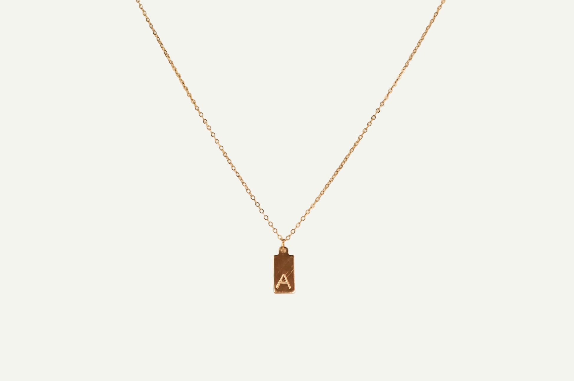 Gold necklace with a pendant featuring the letter 'A' on a white background